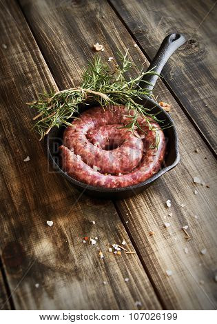 raw beef sausages on a cast-iron pan with rosemary and spices,  wooden table, selective focus
