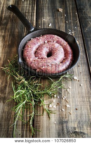 raw beef sausages on a cast-iron pan with rosemary and spices,  wooden table, selective focus