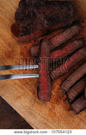 grilled beef fillet steak on fork over wooden board served with different kind of dry spices salt crushed black pepper hot baked sweet paprika red hot chili on dark table