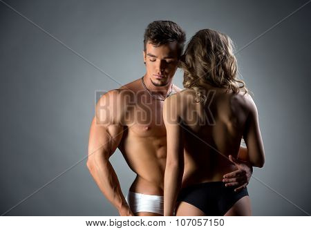 Muscular hunk embracing topless model by waist