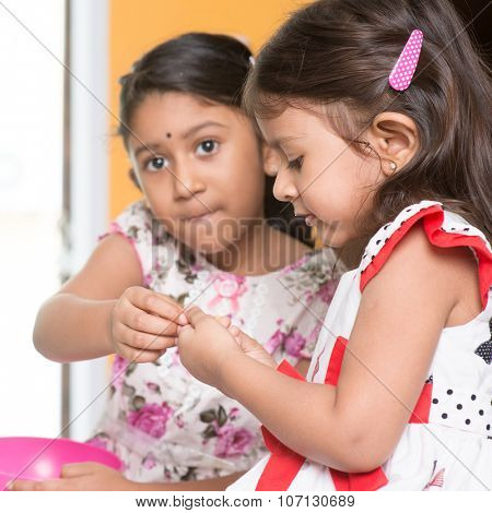 Candid shot of Indian girls sharing traditional snack murukku with each other. Asian sibling or children eating food, living lifestyle at home.