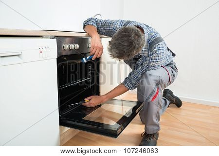 Repairman Examining Oven With Flashlight