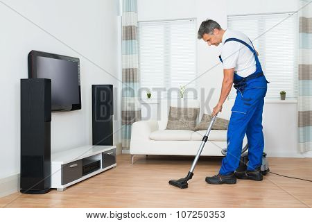 Worker Cleaning Floor With Vacuum Cleaner In Living Room
