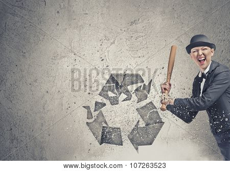 Young emotional woman crashing recycling sign with baseball bat