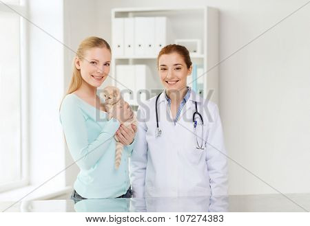 medicine, pet, animals, health care and people concept - happy woman and veterinarian doctor with stethoscope checking scottish fold kitten up at vet clinic