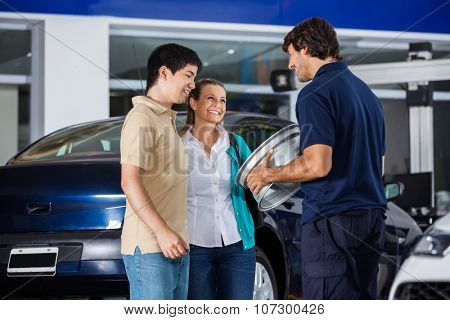 Happy male technician showing metallic hubcap to couple at garage