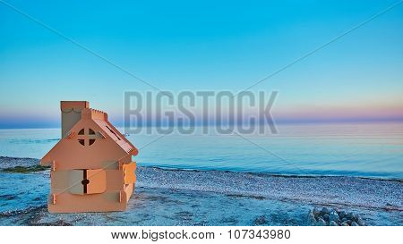 Toy house made of corrugated cardboard in the sea coast at sunset.