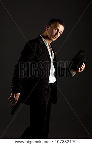 Sexy man posing as mafiosi, on gray background