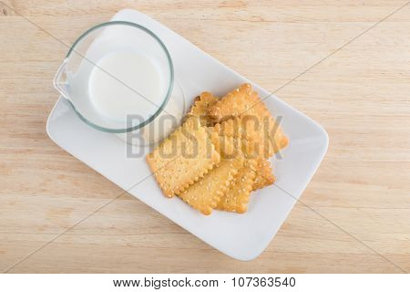 Fresh milk in glass jug and biscuits placed in a white dish on wooden background
