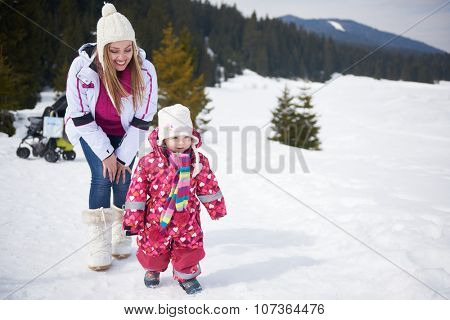 happy family on winter vacation, mom and cute little girl have fun and slide while snow falkes falling