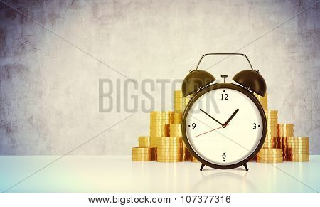 An Alarm Clock And Golden Coins Are On The Table In A Room With Concrete Wall. A Concept Of Time Man