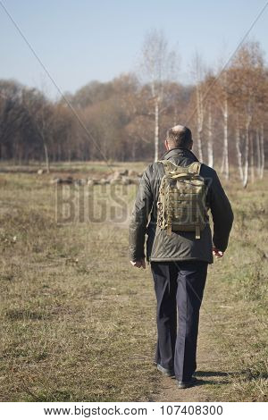 man with a backpack on his shoulders walking on path in park