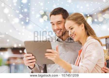 shopping, technology and people concept - happy couple with tablet pc taking selfie in mall or business center with snow effect