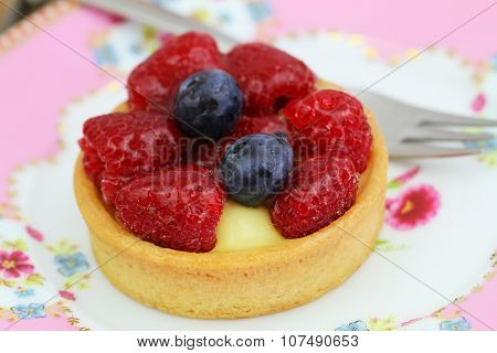 Delicious crunchy tartelette with custard, fresh raspberries and blueberries, closeup