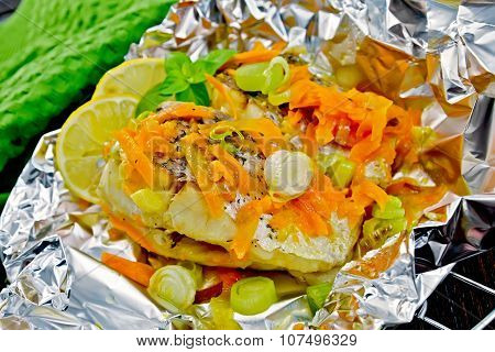 Pike with carrots and leeks in foil on dark board