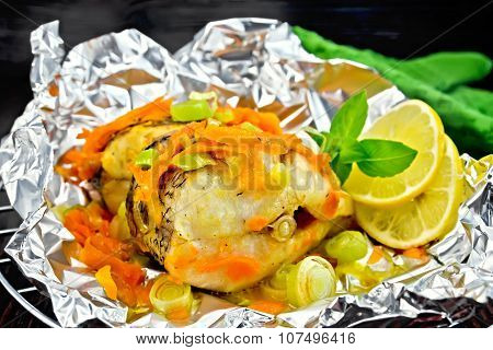 Pike with carrots and onions in foil on dark board