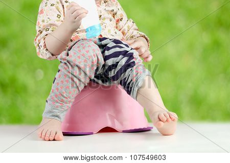 Children's Legs Hanging Down From A Chamber-pot On A Green  Background