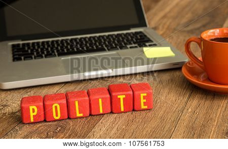 Polite written on a wooden cube in front of a laptop