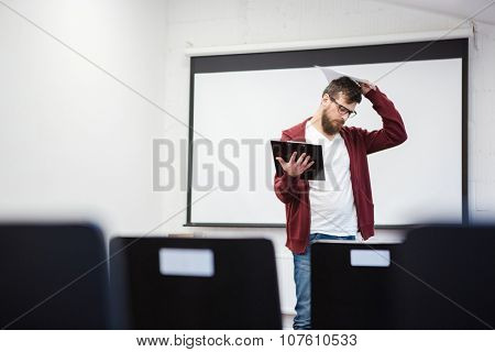 Young teacher with beard in brown hoodie thinking in empty classroom near the whiteboard