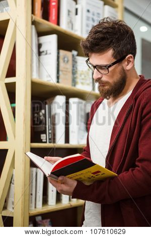 Handsome young student in glasses and brown hoodie reading book in library