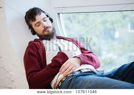 Handsome young guy listening to music and sleeping on the white window sill