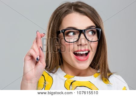 Portrait of a cheerful woman with crossed fingers looking away isolated on a white background