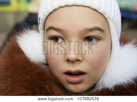 Portrait of brown-eyed girl (9-10 years) in a knitted hat and fur jacket