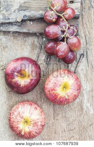 Apple and red grape sited on the old wooden floor.
