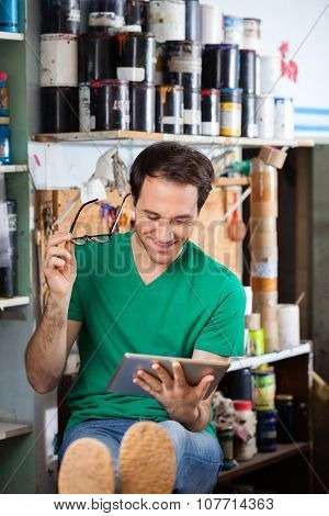 Smiling male worker holding eyeglasses while using digital tablet in paper factory
