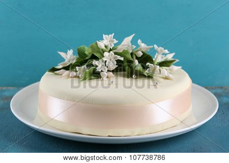 Cake with sugar paste flowers on color wooden background