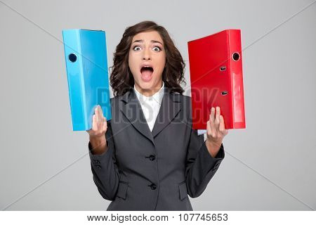 Crazy hysterical pretty curly young woman in gray jacket screaming and holding blue and red binders