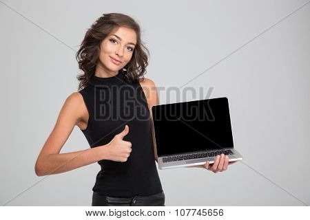 Happy beautiful smiling young female showing blank laptop computer screen and thumbs up
