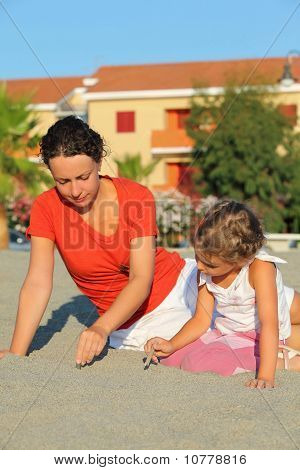 Мать с дочерью в дневное время сидеть на пляже и опираться на песок палочки