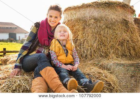 Portrait Of Happy Woman With Cute Child Sitting On Hay On Farm