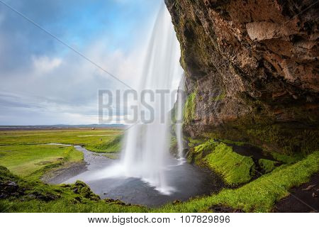 Seljalandsfoss waterfall in July. Passage under the waterfall. Sunny day in Iceland