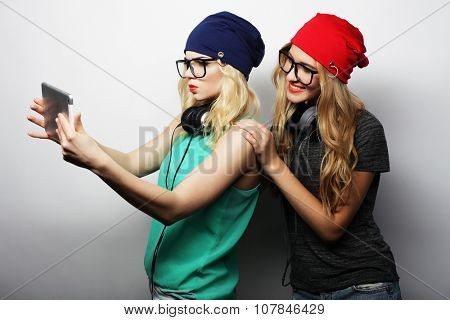 two hipster girls friends taking selfie with digital tablet, studio shot over gray vackground