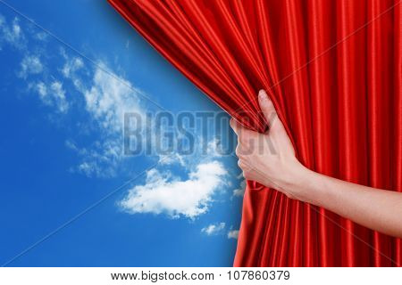Human hand opens red curtain on sky background