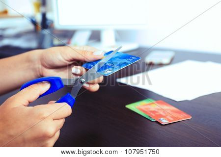 Woman's hands cutting bank card with scissors on wooden table background