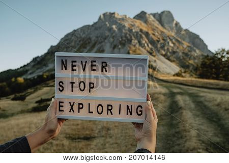 Box with text never stop exploring in woman hands against the background of the mountain. Travel concept