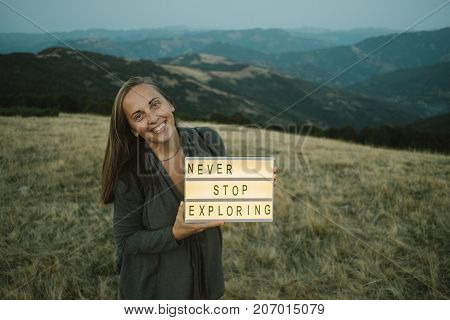 Happy Woman With Box With Text Never Stop Exploring  Against The Background Of The Mountain. Travel