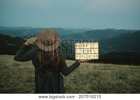Back Of Woman With Box With Text Never Stop Exploring  Against The Background Of The Mountain. Trave