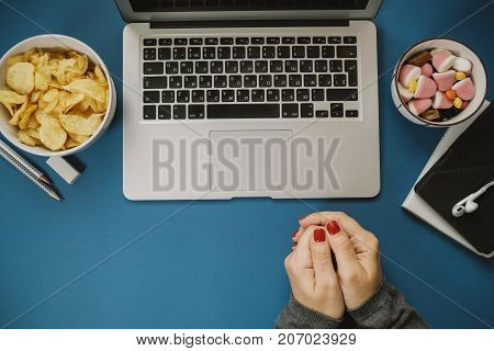 Work Space With Woman Hands Near Laptop With Unhealthy Food: Candy And Chips On Blue Background. Top