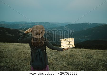 Back Of Woman With Box With Text Never Stop Exploring  Against The Background Of The Mountain. Trave