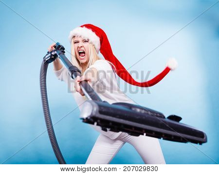 Woman vacuuming the house last minute. Teen girl in santa helper hat with vacuum cleaner angry furious face expression. Christmas time and housework concept.