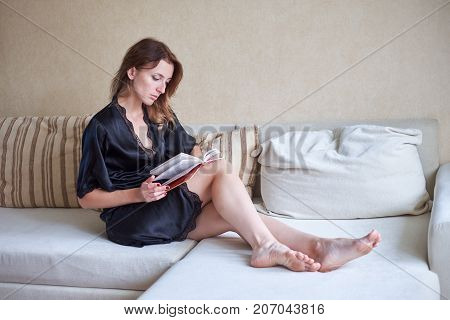 White cozy bed and a beautiful girl, reading a book, concepts of home and comfort.