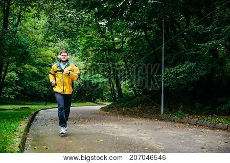 man runnin in autumn park with music in rainy weather