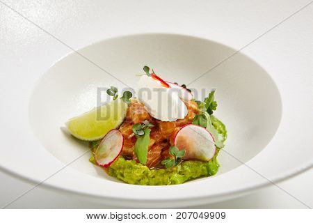 Menu in Pan-Asian cuisine - Tartar from salmon with avocado cream cheese chili pepper and fresh greens in the white bowl