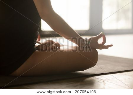 Mudra gesture close up image, mental peace and concentration concept, woman practicing yoga at home, sitting in Padmasana exercise, Lotus pose, working out, wearing sportswear, studio floor background