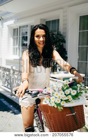 Eastern girl sitting on bicycle with flowers in backet,house on background,summer