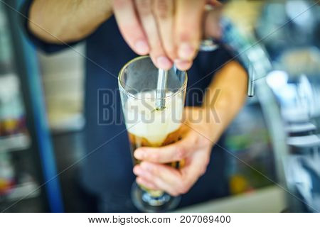 Close-up of young bartender pouring beer while standing at the bar counter.
